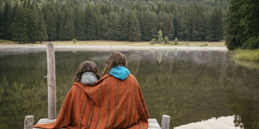 Mother and daughter sitting on a jetty with lake and forest in front